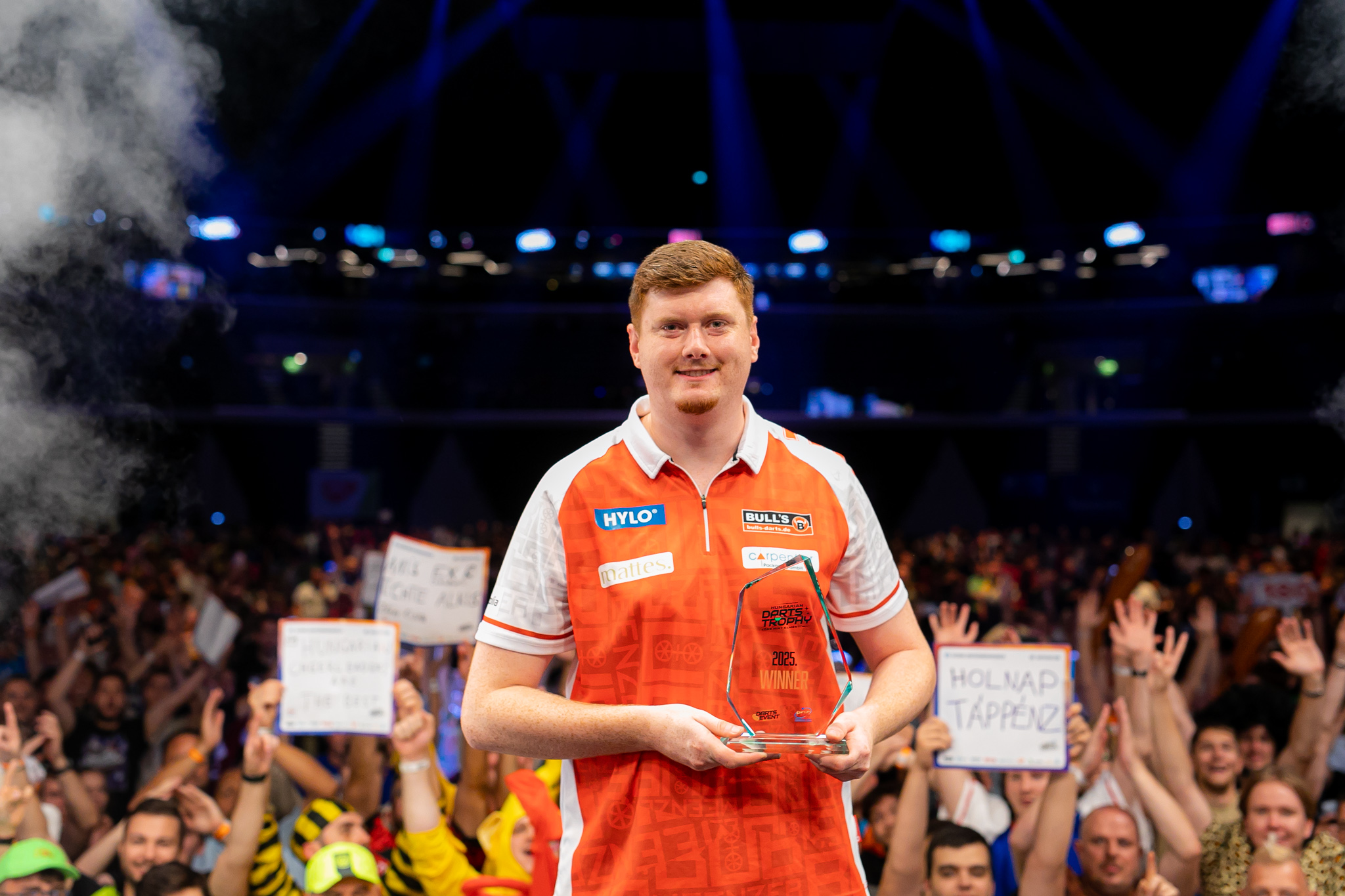 Niko Springer posiert lächelnd als stolzer Sieger der Hungarian Darts Trophy 2025 mit Trophäe vor jubelndem Publikum in Budapest