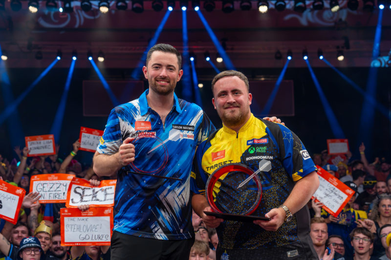 Luke Humphries und Luke Littler posieren als Runner-up und Sieger der Czech Darts Open 2026 mit Trophäen vor jubelndem Publikum in Prag